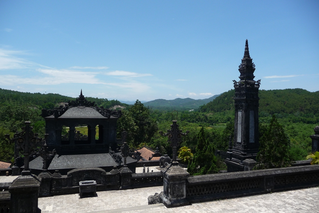 A dark concrete stele pavilion and terrace at the Khai Dinh tomb, looking out over pine-covered hills near Hue