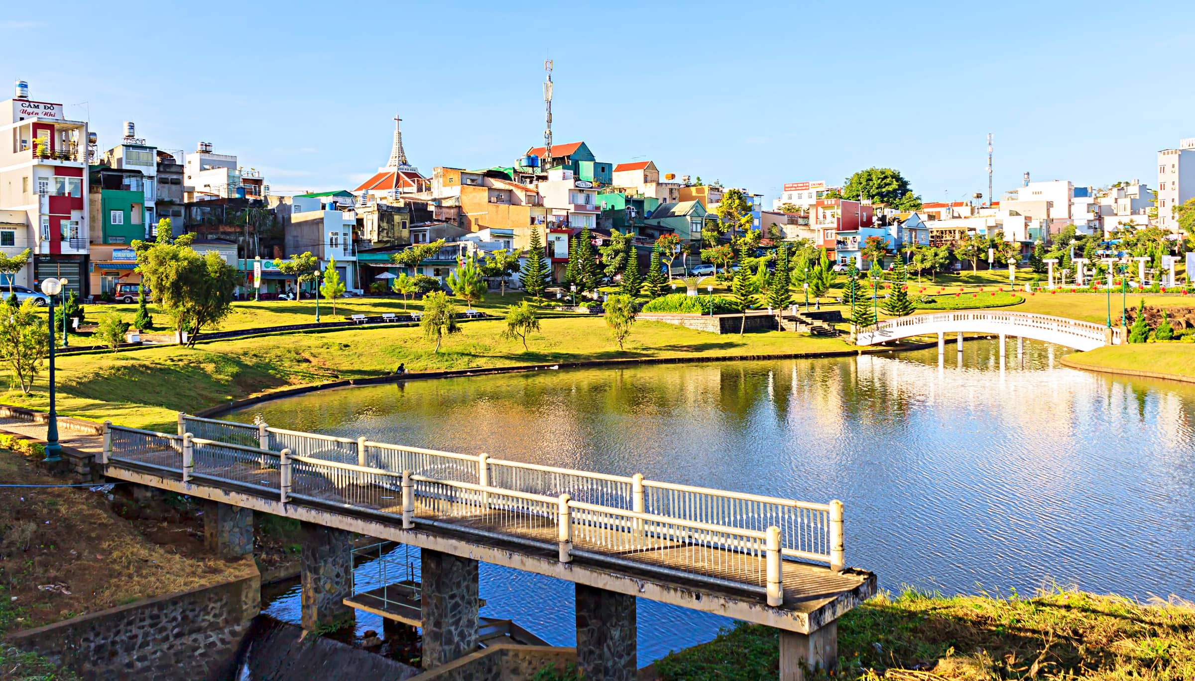 A footbridge over the lake in the park at Bao Loc with the town's houses behind