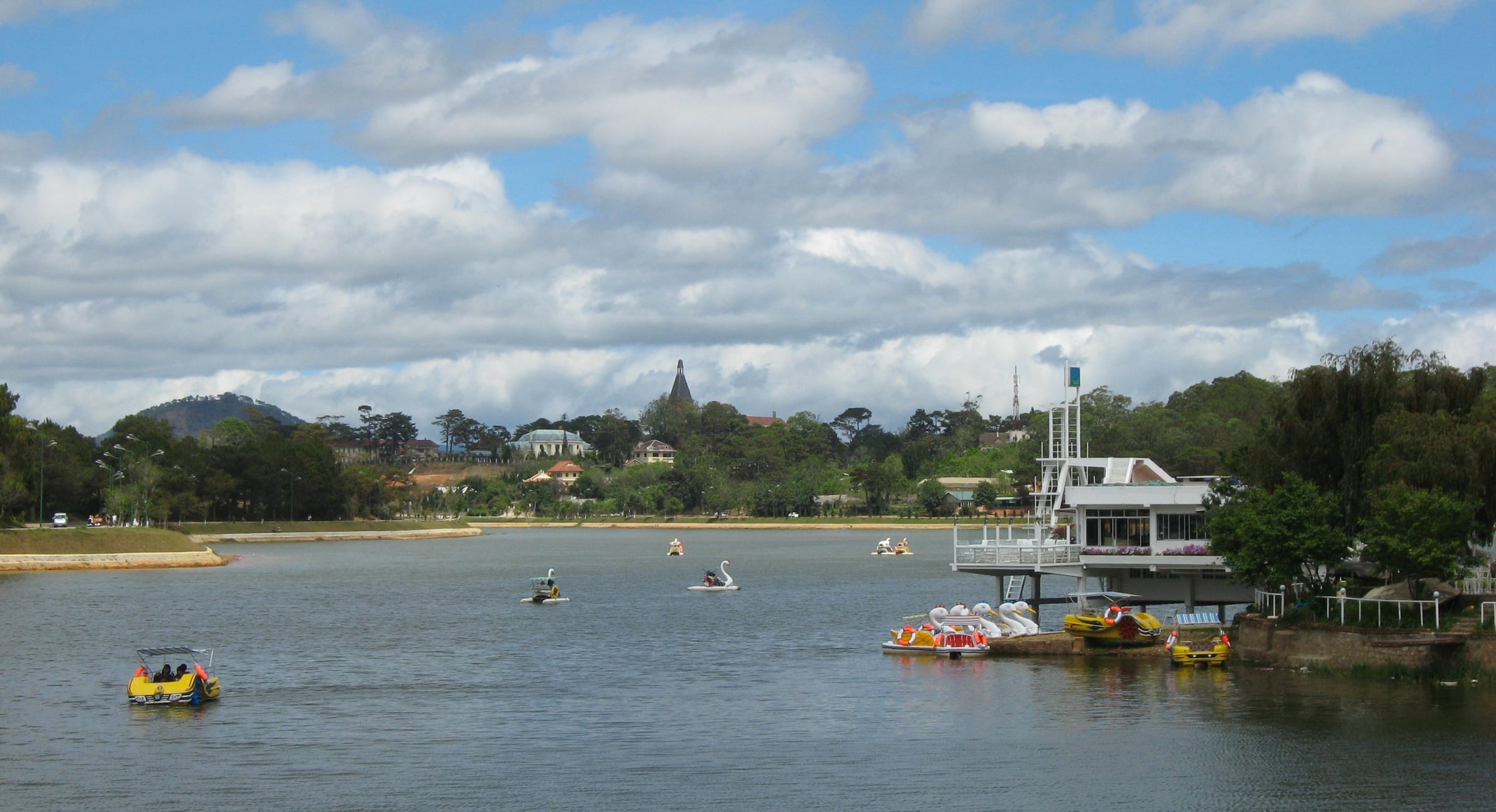 Pedal boats and the pine-fringed shore of Xuan Huong Lake in central Da Lat under big clouds