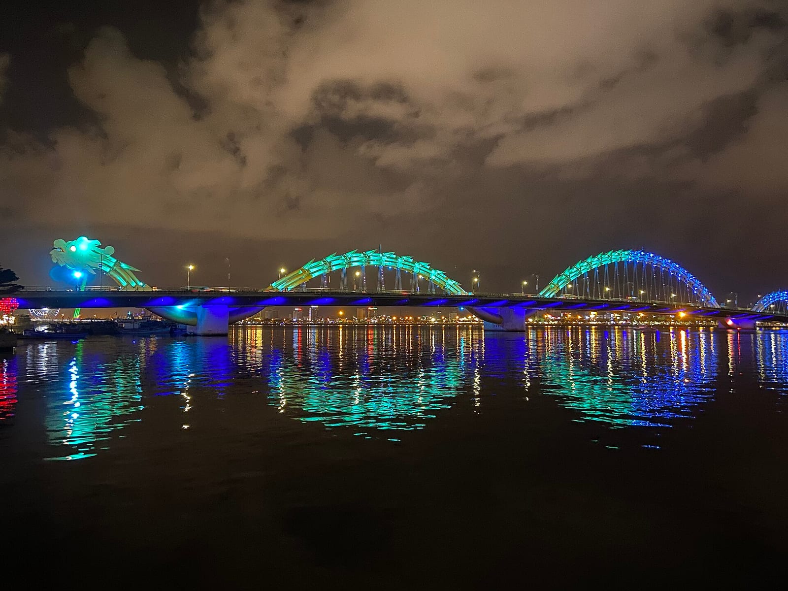The Dragon Bridge in Da Nang lit up in green at night, reflected in the Han River