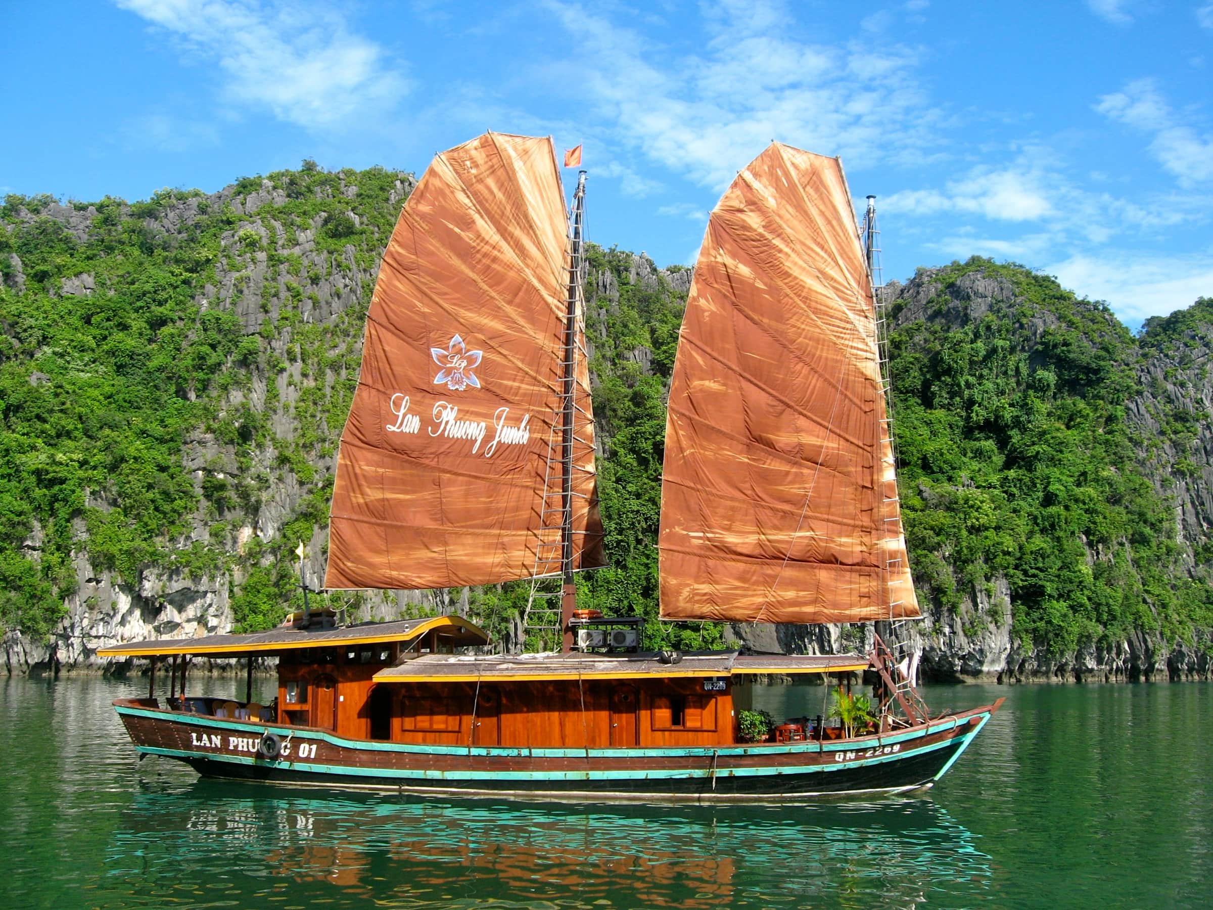 A traditional wooden junk with orange sails among the limestone islands of Ha Long Bay