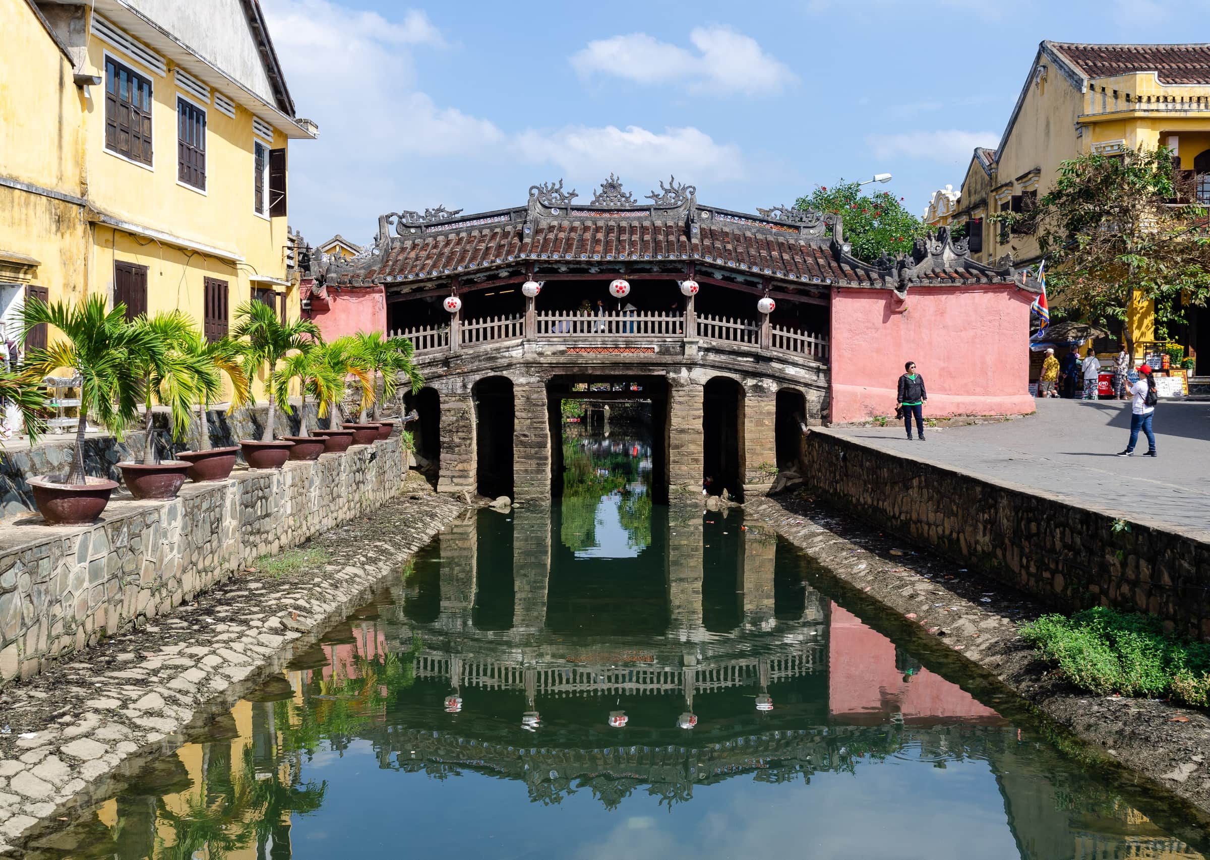 The Japanese Covered Bridge in Hoi An reflected in the canal, with yellow-washed old town houses beside it