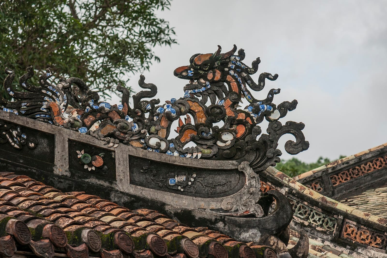 A carved stone and ceramic dragon along the roofline of a royal tomb near Hue