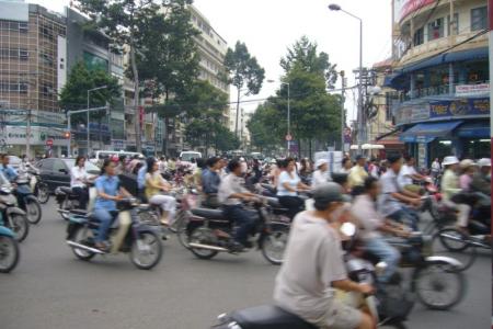 Motorbikes and a few cars moving through a busy Saigon junction