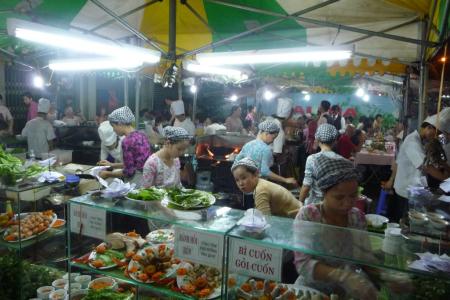 Diners packed at tables under a striped awning at a Saigon night market